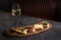 Four bruschettas lay on wooden board. Appetizers with tomato, mozzarella, pesto, salmon and roast beef. A glass of white wine on Royalty Free Stock Photo