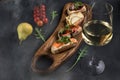 Four bruschettas lay on wooden board. Appetizers with tomato, mozzarella, pesto, salmon and roast beef. A glass of white wine on Royalty Free Stock Photo