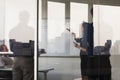 Four business people standing and looking at a white board on the other side of a glass wall