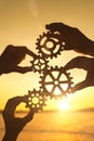 Four businessmen`s hands collect a puzzle of gears against the sunset.