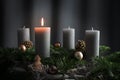 Four candles, one of them lit on an advent arrangement from fir branches and Christmas ornaments, holiday decoration against a
