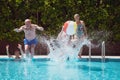 Four carefree people playing in outdoor swimming pool jumping and splashing water. Summer and holiday concept Royalty Free Stock Photo