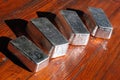 Four cast silver unmarked bars on a mahogany background.