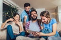 Four casual happy friends laughing shopping online together in a tablet sitting on a sofa in the living room