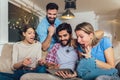 Four casual happy friends laughing shopping online together in a tablet sitting on a sofa in the living room