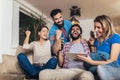 Friends laughing shopping online together in a tablet sitting on a sofa in the living room at home Royalty Free Stock Photo