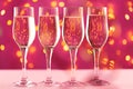 Four champagne glasses against pink background with blurred garland Royalty Free Stock Photo