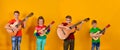 Four children with acoustic guitars in bright and colorful clothes stand in a row on a yellow background Royalty Free Stock Photo