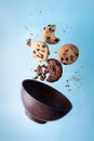 Four chocolate chip cookies and a bowl flying on a blue background