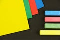 Four colored children crayons and papers on black background, top view, yellow chalk and paper select Royalty Free Stock Photo