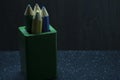 Four colored large pencils in a large green box on a dark background