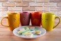 Four colored tea, cofee cups with drawn eyes staying around white dish with marshmallow pieces and looking on them Royalty Free Stock Photo