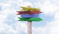 Four colored wooden arrows pointers yellow, red, blue and green. Blue sky background with clouds