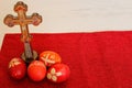 Four colorful Easter eggs next to Christian wooden cross on red background