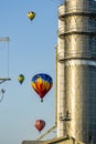 Four colorful hot air balloons dramatically fly near power lines and metal grain silo in this . Royalty Free Stock Photo