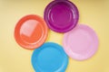 Four colourful plastic plate dishes over yellow beige background. Orange. Purple. Blue. Pink Royalty Free Stock Photo