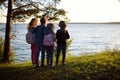 Four cute little sibling standing by the lake enjoying beautiful sunset view. Children exploring nature. Royalty Free Stock Photo