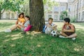 Cute multicultural schoolkids sitting on lawn and tree, speaking and reading books