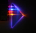 Four different light beams are refracted and mirrored internally a triangular 90 degrees prism on a dark background