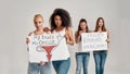 Four diverse women looking at camera while holding, standing with banners in their hands over grey background