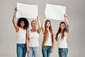 Four diverse women looking at camera while holding, standing with blank banners in their hands over grey