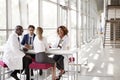 Four doctors talking at a table in a modern hospital lobby Royalty Free Stock Photo