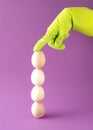 Four eggs arranged vertically are held by a hand in green glove. Easter decoration on purple background Royalty Free Stock Photo