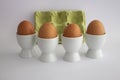 Four eggs in white eggs cups, on white isolated background with yellow carton egg box. Royalty Free Stock Photo