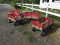 Four empty red wagons by white picket fence in farm driveway, waiting to be used