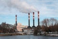 Four factory chimneys emit puffs of smoke against the blue sky.