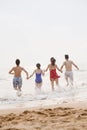 Four friends running into the water on a sandy beach, rear view Royalty Free Stock Photo