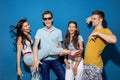 Four good-looking friends are laughing while standing in front of the blue wall having confident and happy looks