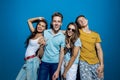 Four good-looking friends are laughing while standing in front of the blue wall having confident and happy looks