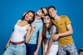 Four good-looking friends are laughing while standing in front of the blue wall having confident and happy looks