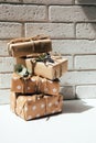 Four handmade gifts in kraft paper, tied with wide twine, decorated with dry flowers on a white table near brick wall