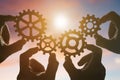 Four hands collect a puzzle of gears, against the background of the sky at sunset. Royalty Free Stock Photo