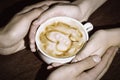 Four hands wrapped around a cup of coffee with heart drawing Royalty Free Stock Photo