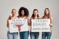 Four happy diverse women looking at camera while holding, standing with banners in their hands isolated over grey Royalty Free Stock Photo
