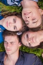 Four happy friends lying together on green grass outdoors Royalty Free Stock Photo