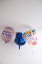 four helium balloons decorated with colored dots and a happy birthday message, with a hanging ribbon, on the roof of a white room Royalty Free Stock Photo