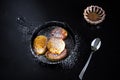 Four homemade fried pancakes in a small cast-iron frying pan. Rose jam. Black wood background.