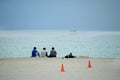 Four humans sitting or lying relaxed on the beach, looking on the endless ocean