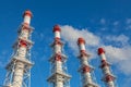 Four industrial chimneys against a blue sky. White smoke comes from several of them