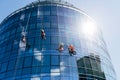 Four industrial climbers clean windows outside a circular business center with mirrored windows. The blue sky is