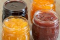 Four jars of different jam on wooden background, closeup