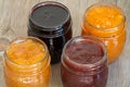 Four jars of different jam on wooden background, top view