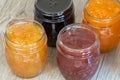 Four jars of different jam on wooden background, top view