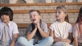 Four kids looking bored and overtired seating on a bench. Royalty Free Stock Photo