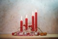 Four lit red candles for the fourth Sunday before Christmas, Advent decoration on a wooden table against a rustic wall, copy space