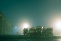 Four lorries parked at a car park, With street lights behind on a moody, atmospheric foggy winters night Royalty Free Stock Photo
